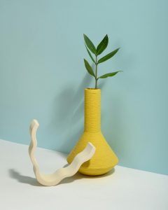A minimalist display with a yellow vase and green leaves against a light blue background.